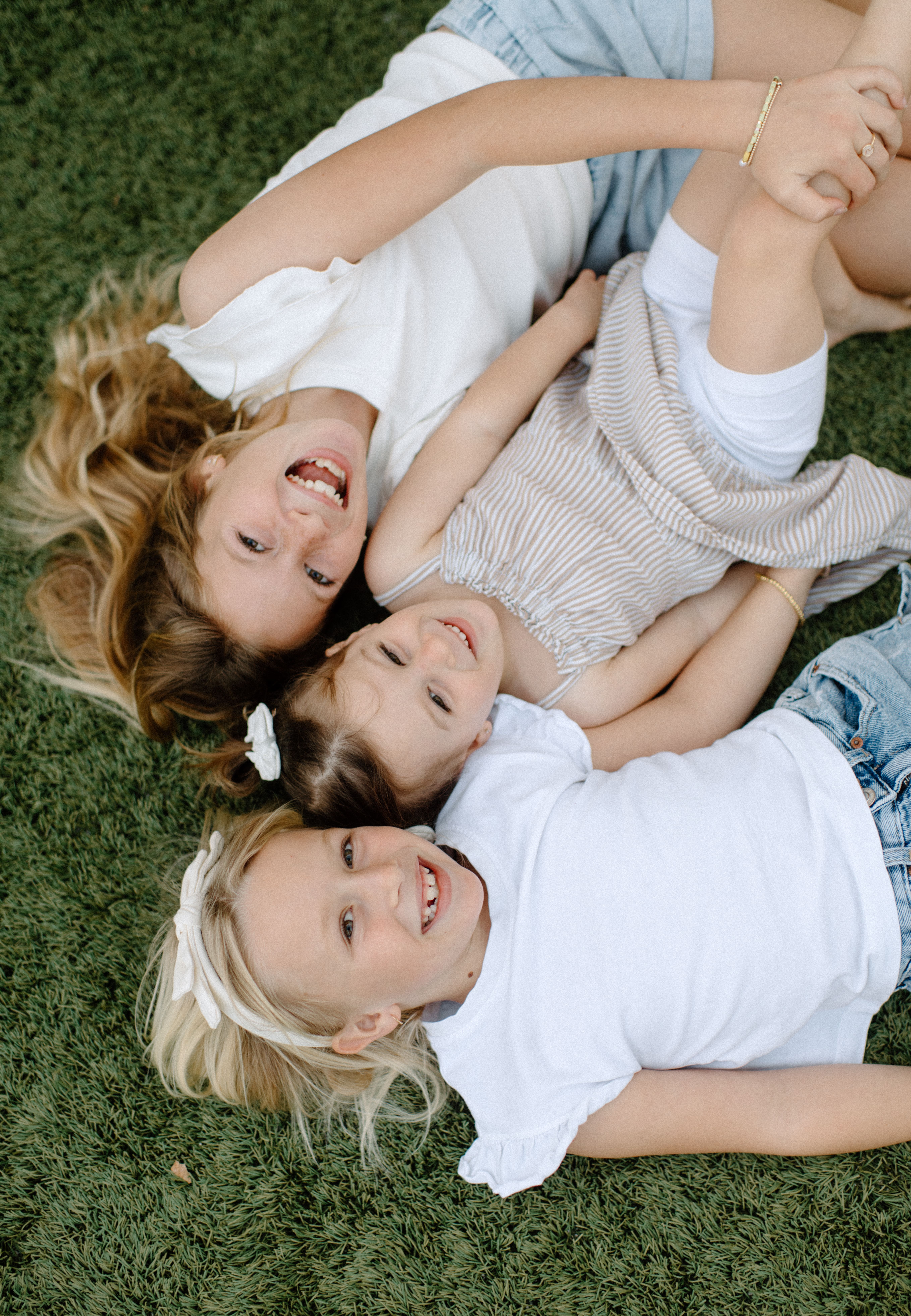 sisters laughing together laying in their grass in their backyard near the Oceanside harbor 