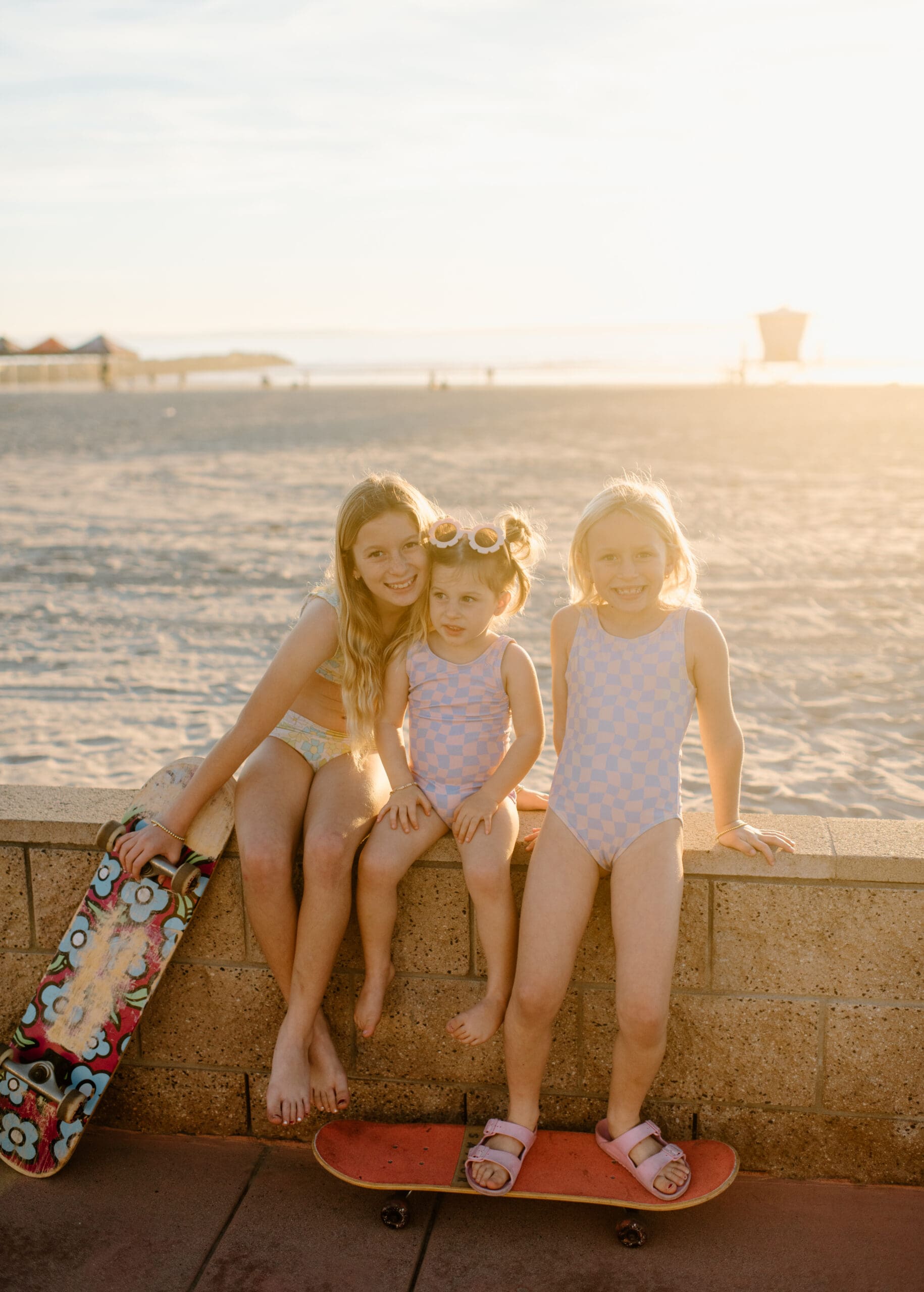 3 sisters sitting on the boardwalk at the Oceanside Harbor with their skateboard